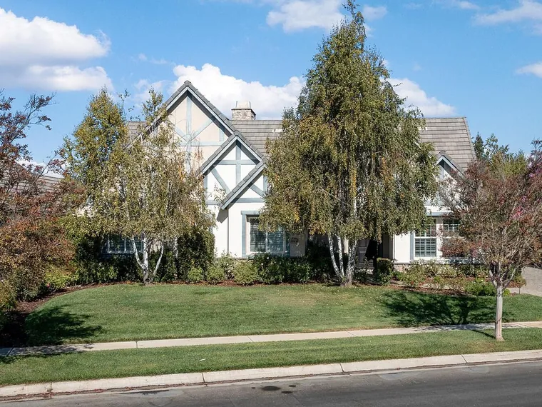 Cream stucco home with blue half timbered gables, a grey tile roof and white birch trees above a sloping lawn at 523 Myrtle Ct, Solvang, CA 93463